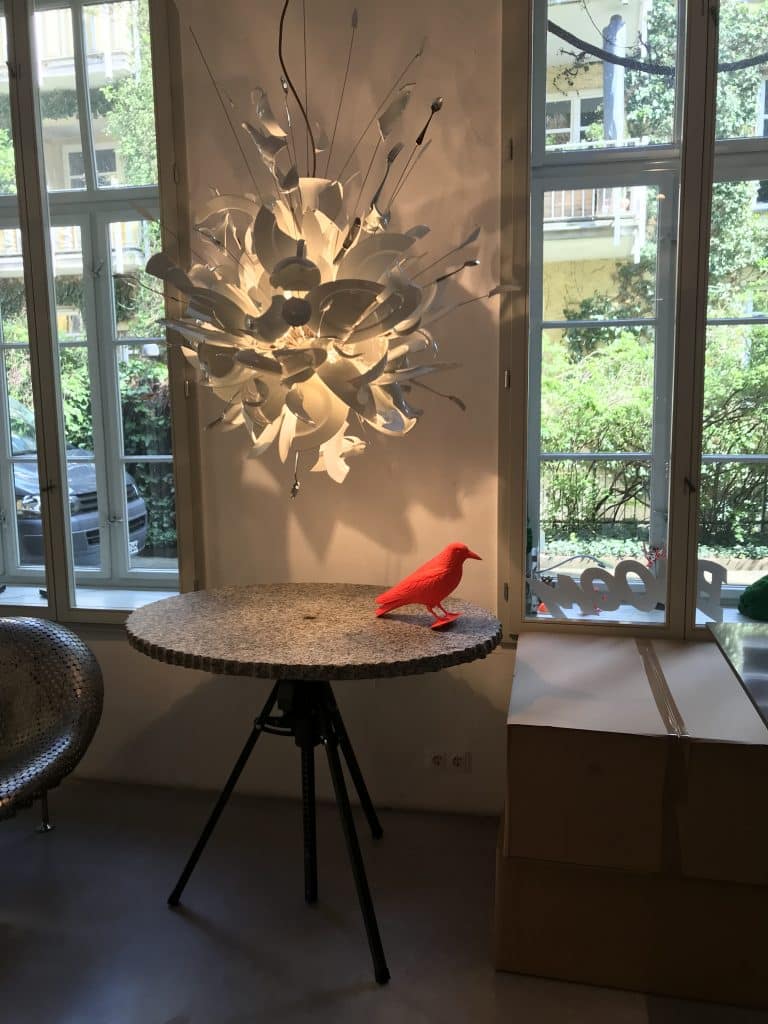 Ausgefallene Ingo Maurer Designer-Pendelleuchte mit Zetteln über einem runden Bistrotisch mit roter Vogelfigur vor Sprossenfenstern zum Garten