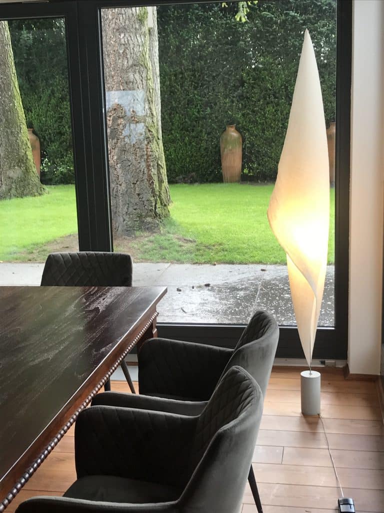 Elegante, segelförmige Ingo Maurer Papier-Stehleuchte neben einem dunklen Holzesstisch mit Armlehnenstühlen vor einer großen Glasfront mit Blick in den Garten