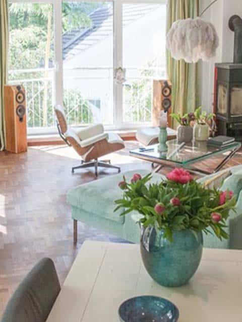 Wohnzimmer mit Designklassikern, grünem Sofa und Blick in den Garten