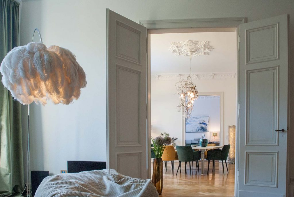 Blick vom Wohnzimmer durch eine Altbau-Flügeltür ins Esszimmer mit skulpturaler Hängeleuchte