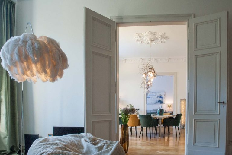 Blick vom Wohnzimmer durch eine Altbau-Flügeltür ins Esszimmer mit skulpturaler Hängeleuchte