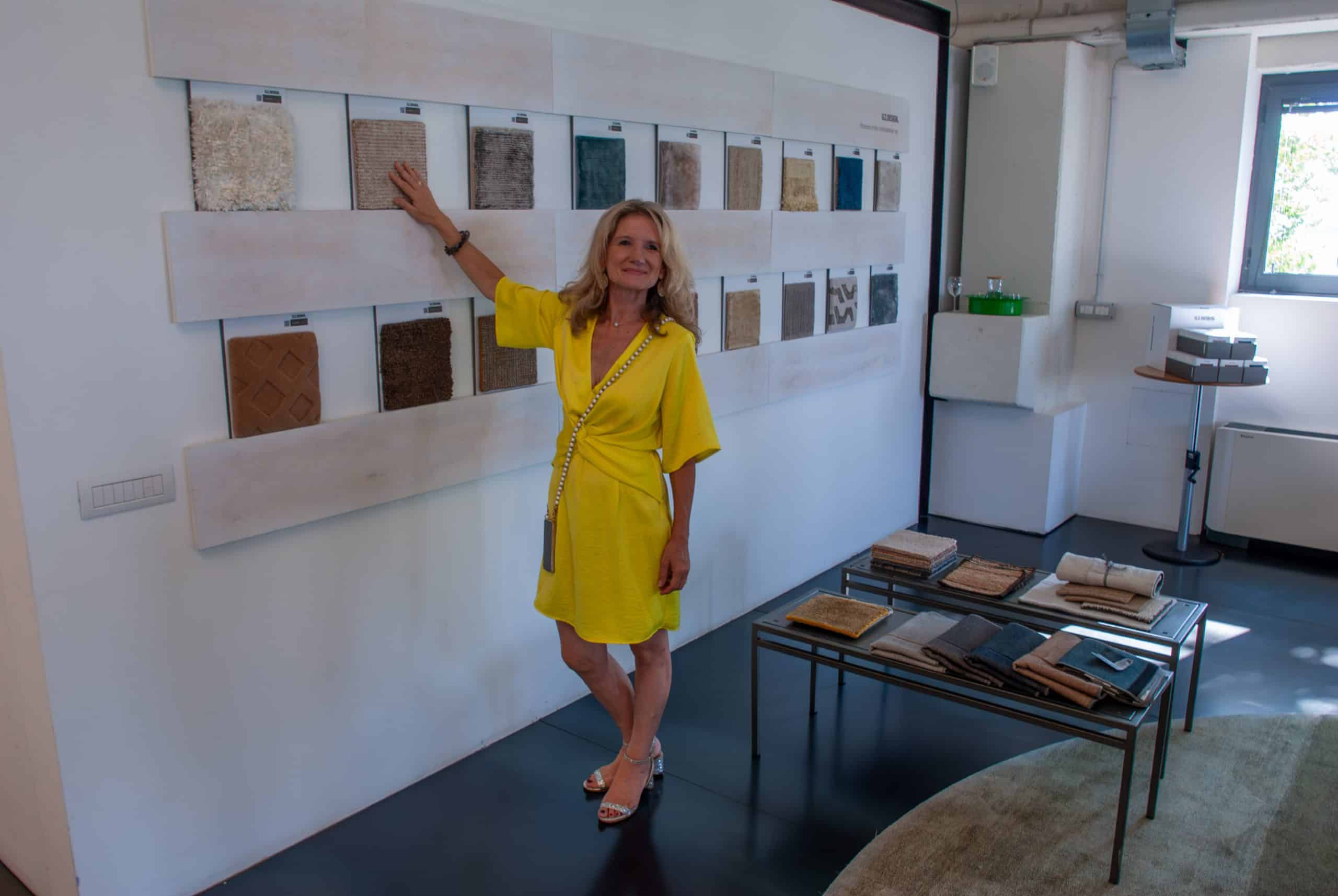 Interior Designerin Susanne Wefers in einem gelben Kleid präsentiert Materialmuster und Farbmuster an einer Wand im Studio